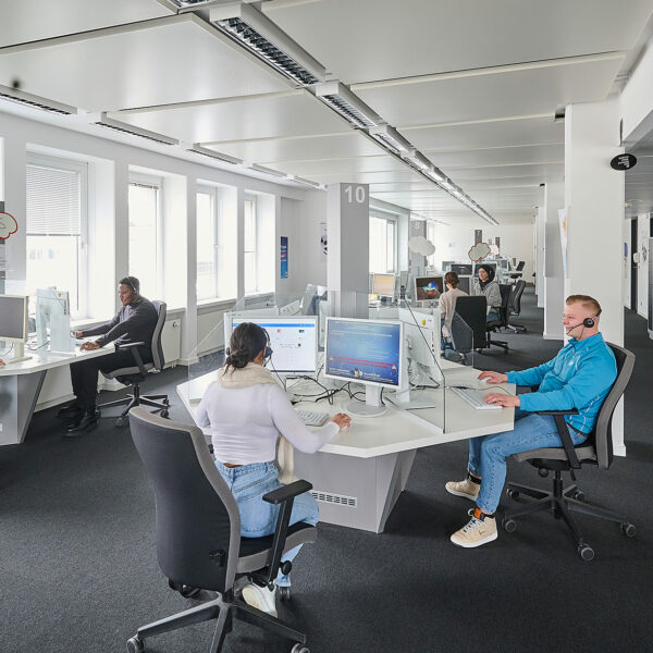 Ein Büro in dem mehrere Schreibtische mit Computern stehen an denen Mitarbeiter arbeiten.